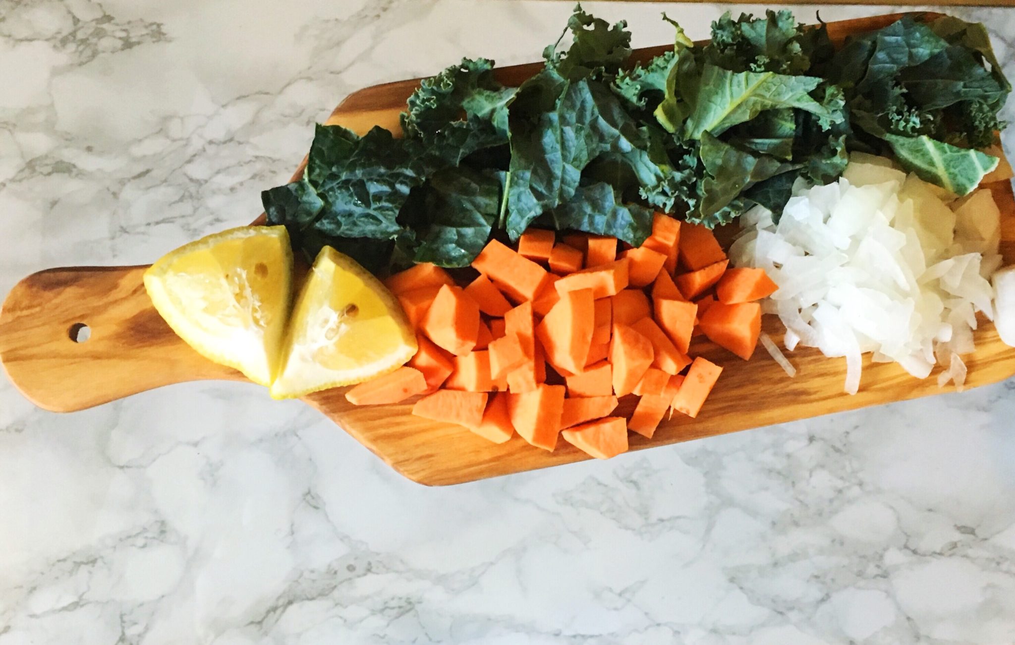 Cutting board with chopped sweet potato, kale, onion, and sliced lemon